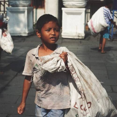 Young boy in poverty carrying a sack of garbage